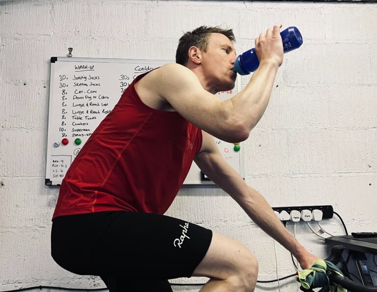A man practicing cycling endurance while sipping from a bottle.