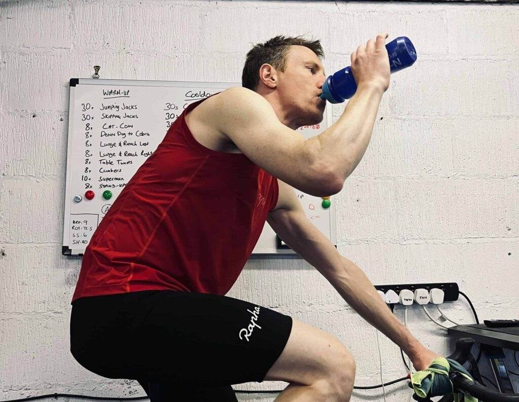 A man practicing cycling endurance while sipping from a bottle.