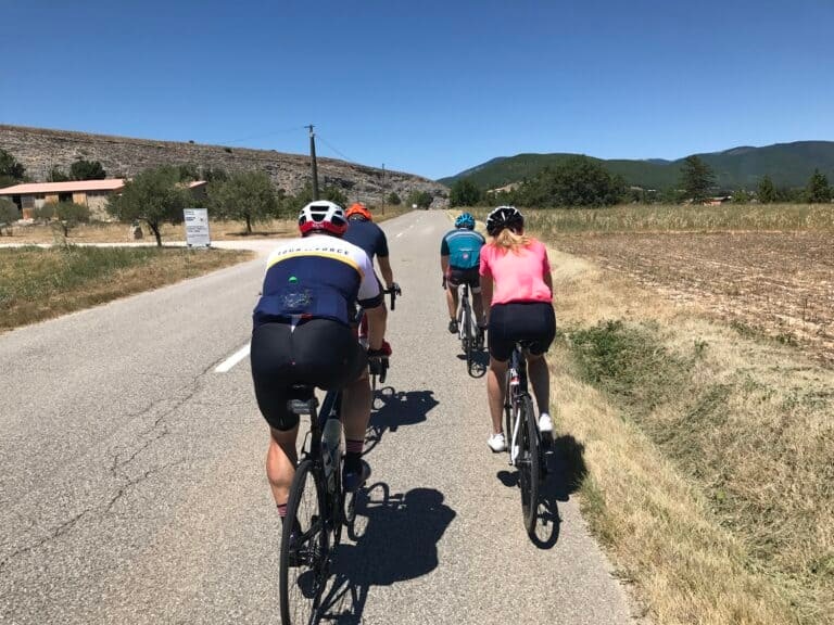 a group of four cyclists riding on a straight country rode
