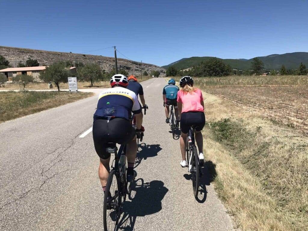 a group of four cyclists riding on a straight country rode