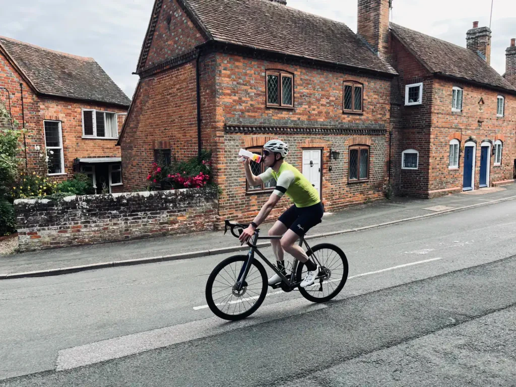 Cyclist drinking water while riding on a street in a residential area.