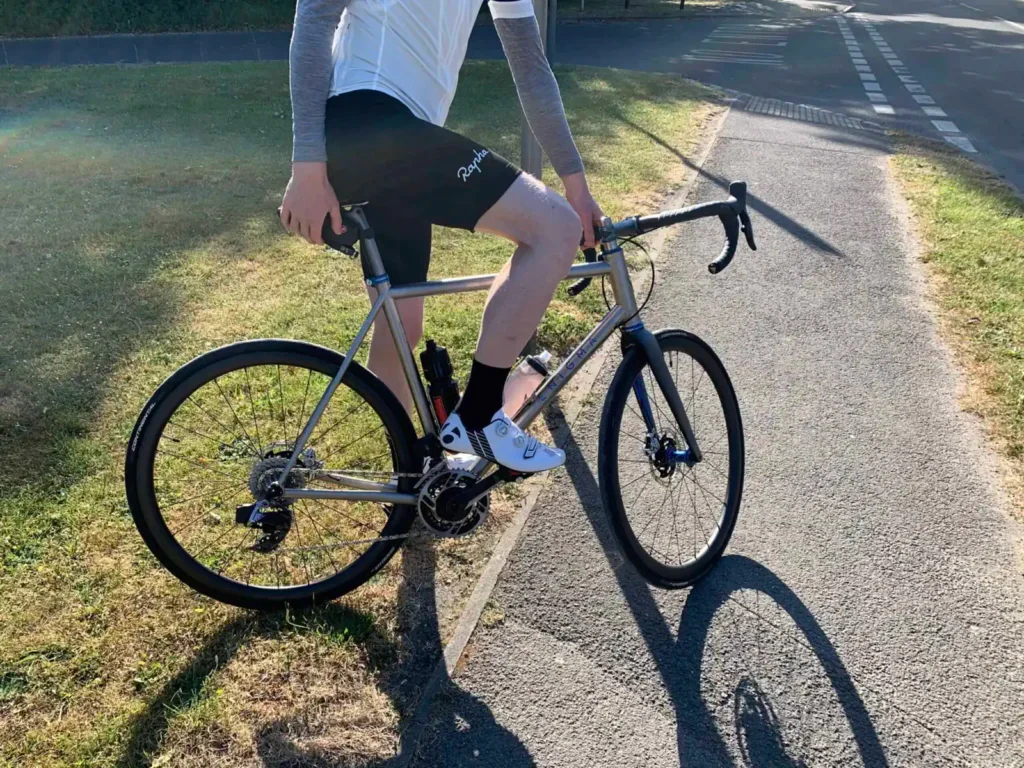 A cyclist straddling a road bike on a sunny day with shadow cast on the pavement.