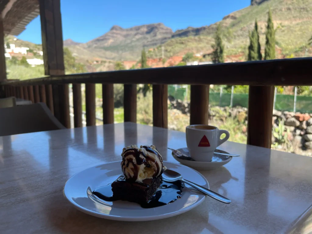 A brownie with ice cream and syrup alongside a coffee at a cycling stop in Gran Canaria offers refreshment amidst breathtaking mountain views.