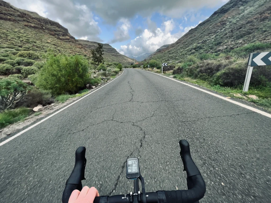 A cyclist navigates the open road amidst Gran Canaria's mountains beneath a cloudy sky.