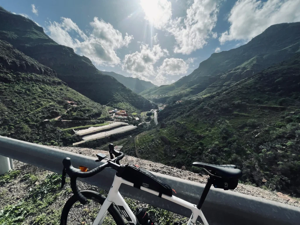 Bicycle perched above a verdant mountain valley in Gran Canaria under a bright sky with scattered clouds.