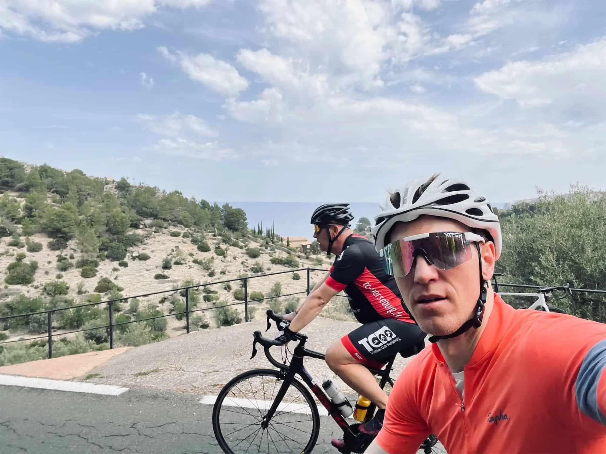 two cyclists riding along a road with sea in background