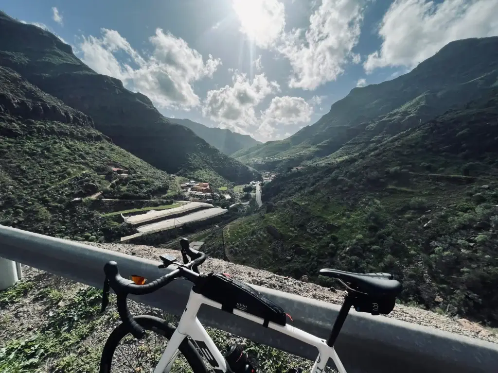 Bicycle perched above a verdant mountain valley in Gran Canaria under a bright sky with scattered clouds.