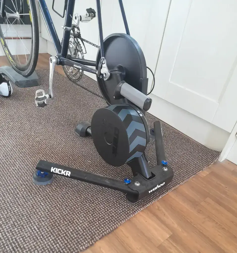 There's a bike hooked up to a Wahoo Kickr indoor trainer, chilling on a carpet next to a white cabinet.