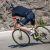 The cyclist, in black gear and helmet, adeptly navigates his green bike on the mountain road, exemplifying the precision of road cycling.