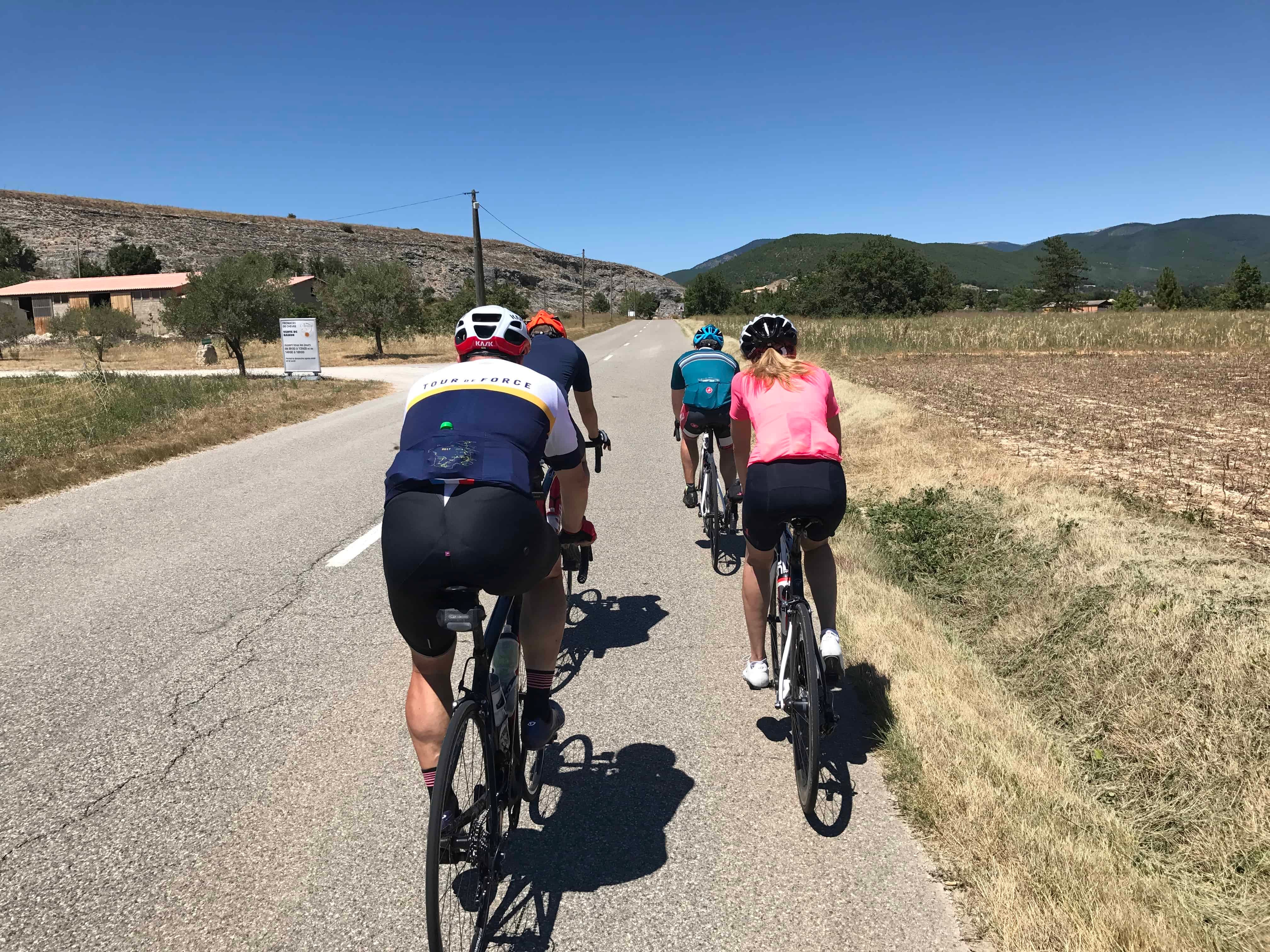 a group of four cyclists riding on a straight country rode