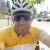 Cyclist Rhys Smith, donning a yellow jersey and sunglasses, smiles for the camera amidst a bustling city street backdrop.