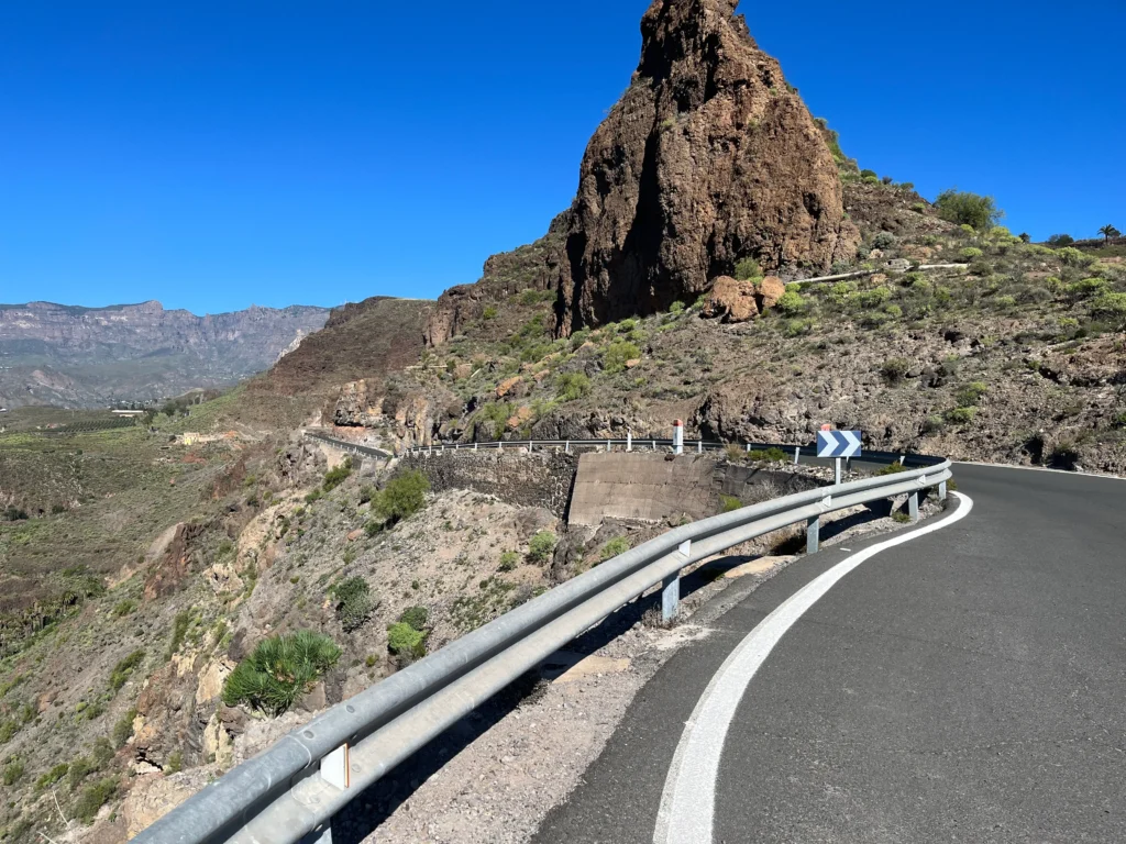 Gran Canaria offers a rugged mountain road with guardrails and cliffs under a clear sky—ideal for cycling enthusiasts favoring rocky terrain and minimal greenery.