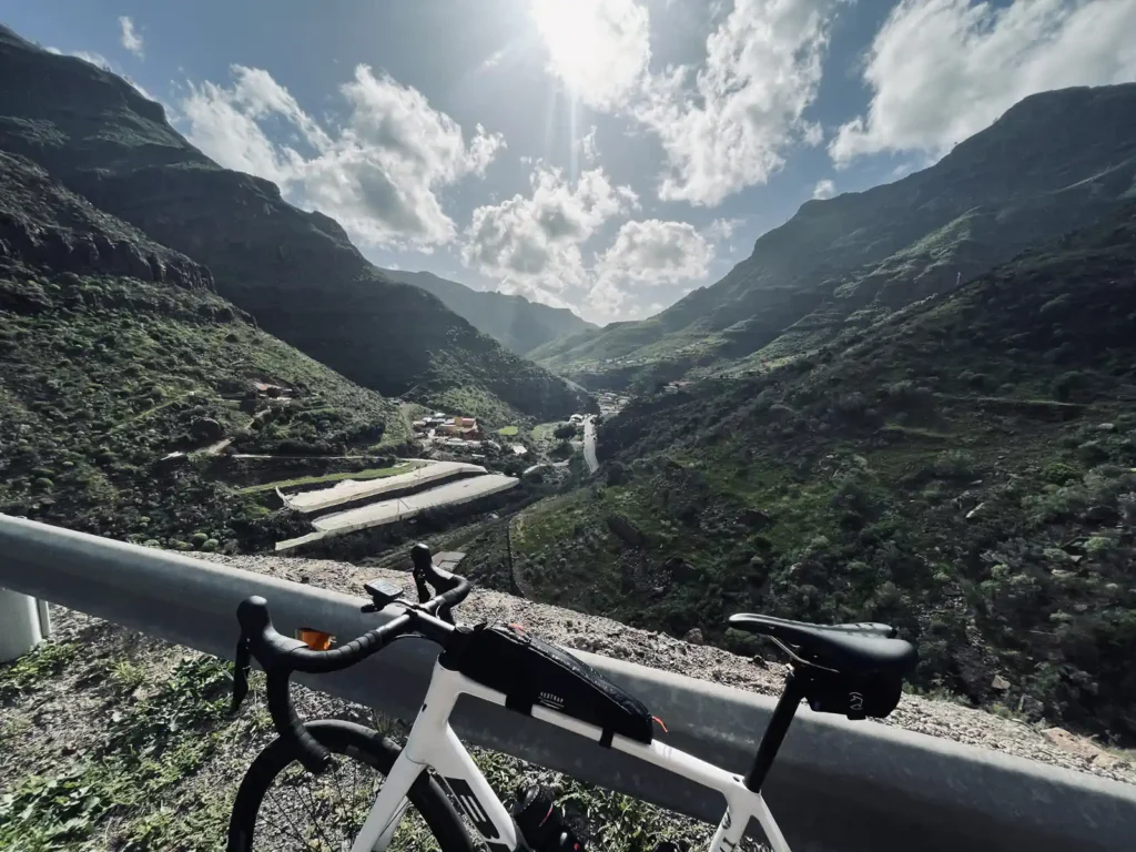 A road bike leaning on a guardrail overlooking a sunlit mountainous landscape with a small village nestled in a valley. A road bike leaning on a guardrail overlooking a sunlit mountainous landscape with a small village nestled in a valley.